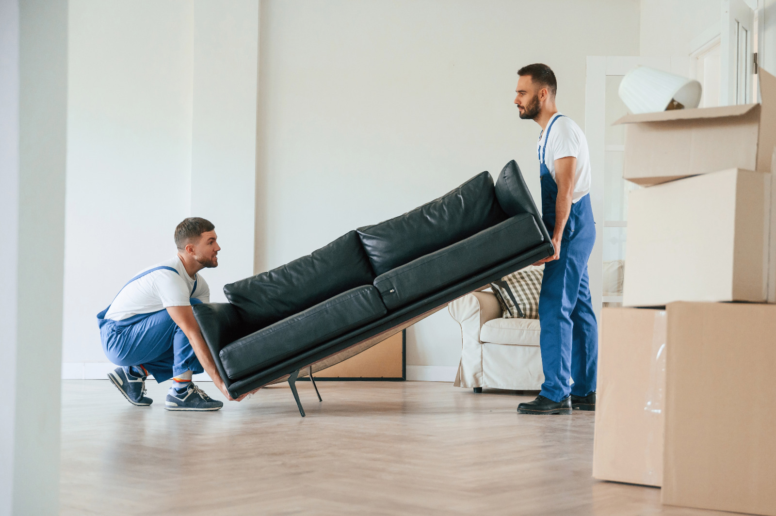 Wood Joyful Restoration in Lee: two movers carefully lifting a sofa onto a newly refinished oak herringbone parquet (solid wood) floor.