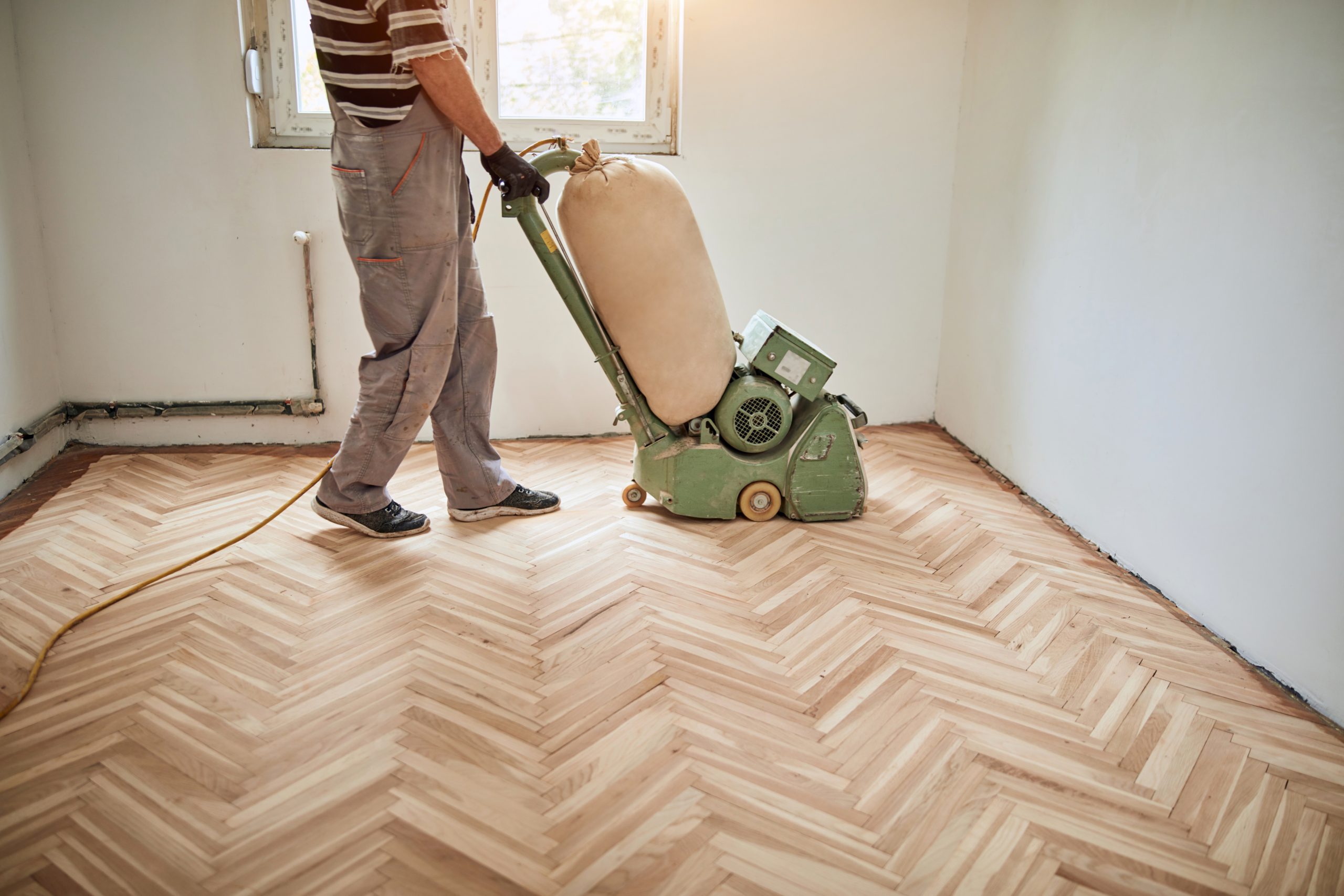 Wood Joyful Restoration in Lee: technician sanding an oak herringbone parquet (solid wood) floor with a belt sander for refinishing.
