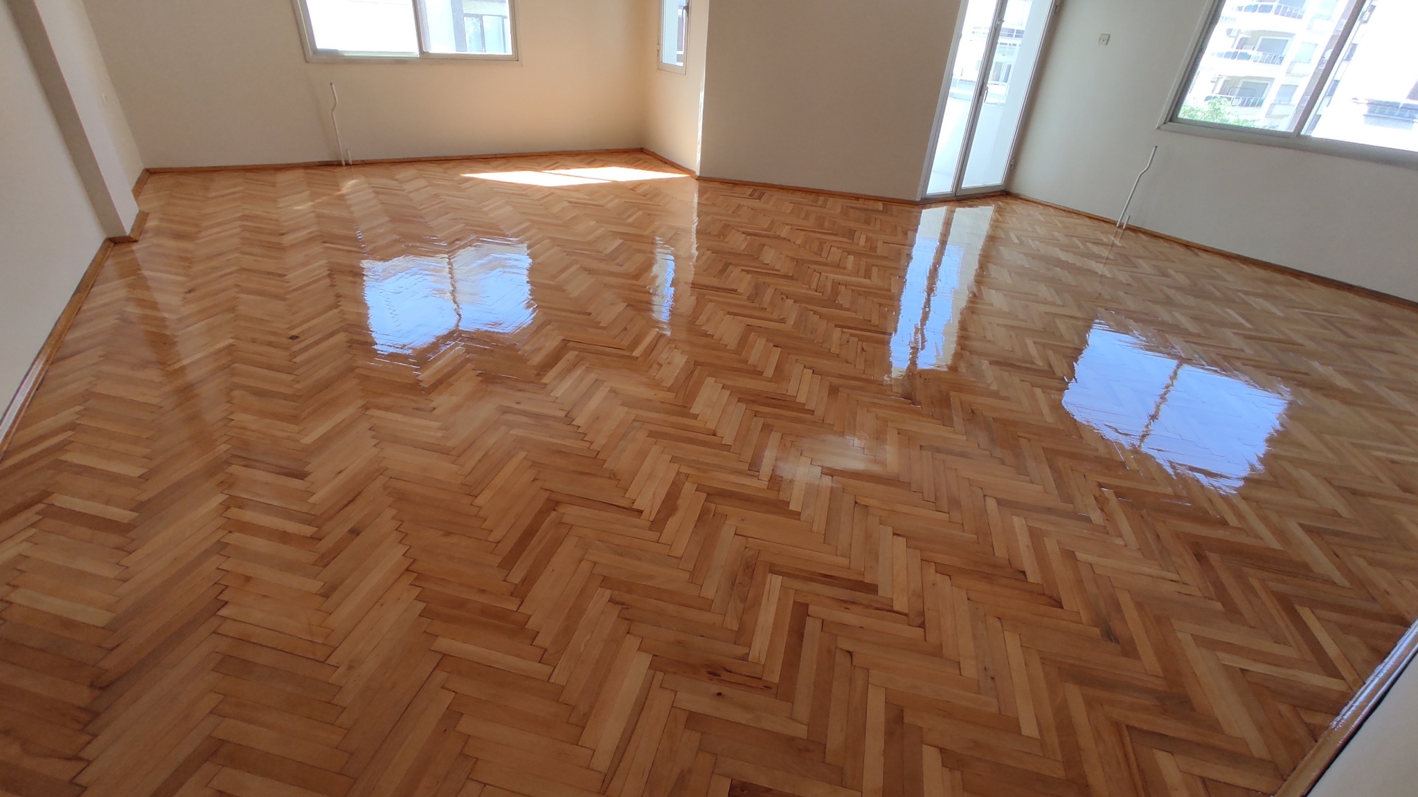 Parquet floor sanding in Lee on a finished oak herringbone parquet floor, showing a smooth, glossy surface reflecting natural light in a bright room.