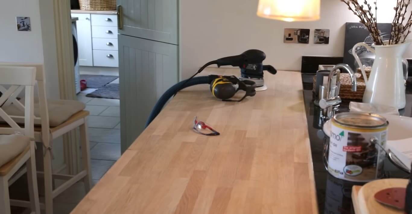 Parquet Floor Sanding specialists in Lee preparing a solid oak wooden kitchen worktop for refinishing, with sander, goggles and oil on the surface.