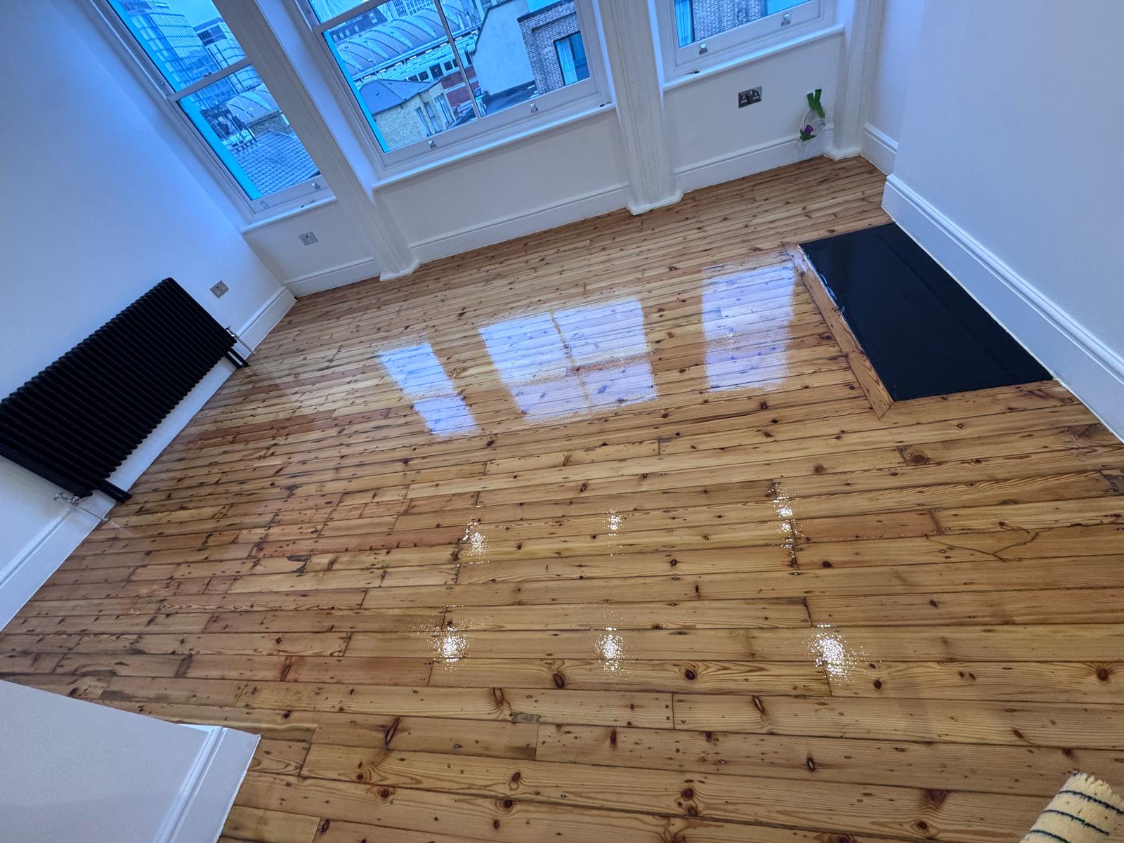 Wood Floor Sanding in Lee on narrow pine softwood floorboards, showing a bright living room with freshly lacquered wooden floor reflecting light from large windows.