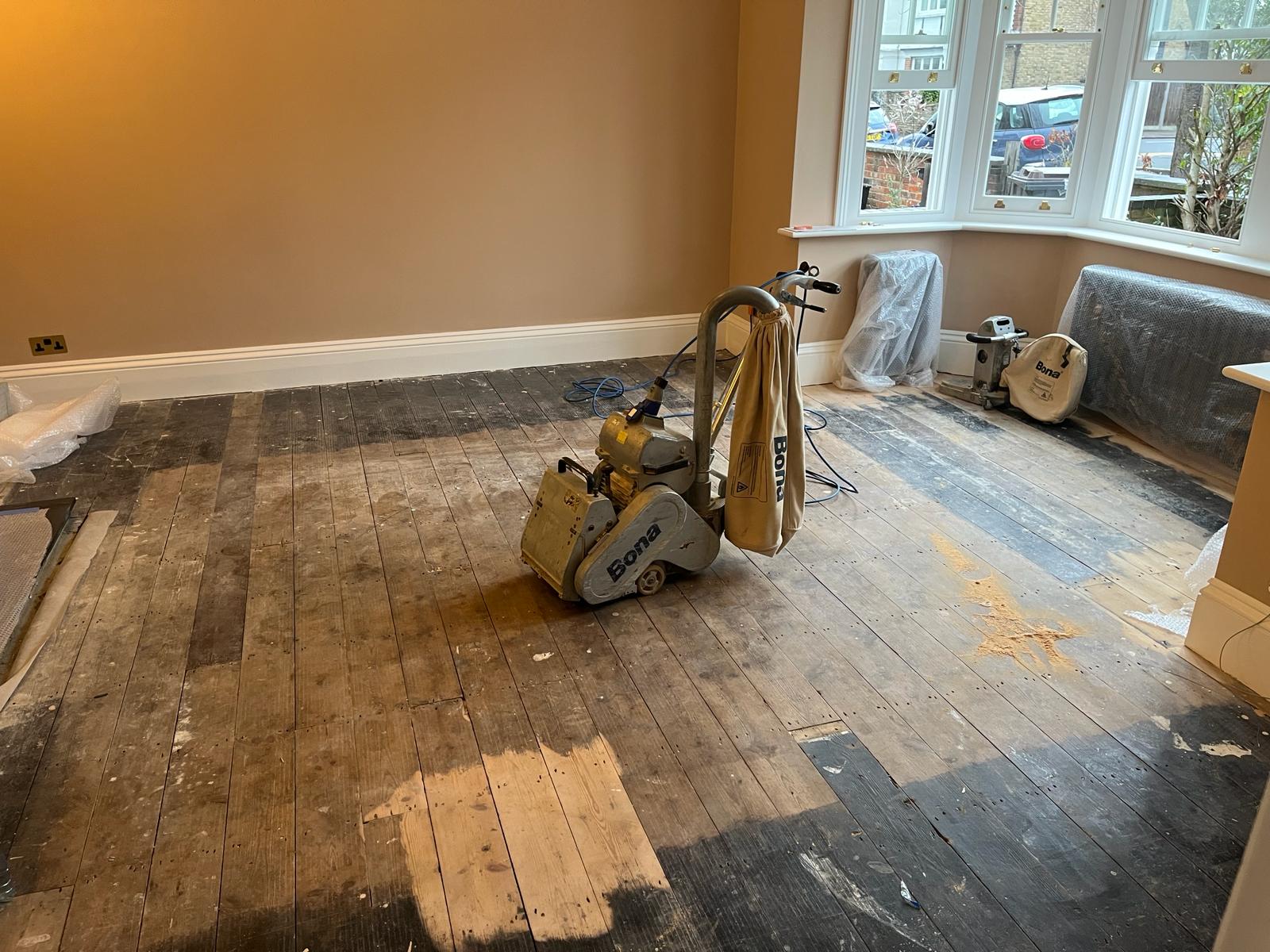 Wood Floor Sanding in Lee on original pine living room floorboards, showing sanding machines in place and the timber surface part-way through restoration.